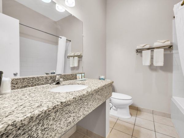 A clean bathroom with a granite countertop, sink, toilet, and tub. Towels are neatly arranged on a rack above the toilet.