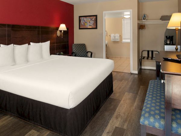 A hotel room with a large bed, nightstands, a chair, desk, TV, open closet area, and warm lighting in a modern, tidy layout.