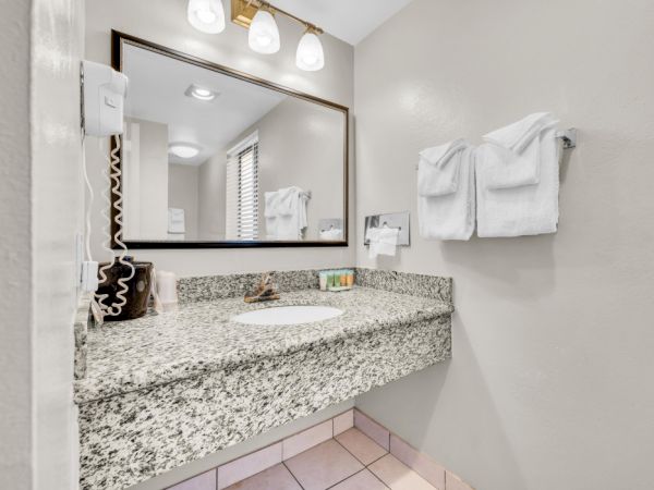 The image shows a bathroom with a granite countertop, a mounted mirror, wall-mounted hairdryer, and neatly folded towels on the wall.