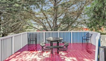 A vibrant red deck features a round table with four seats, surrounded by trees and enclosed by a white railing.