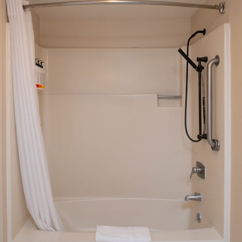A compact bathroom with a bathtub/shower combo, white tile, a overhead curtain, a wall-mounted showerhead, and basic fixtures.