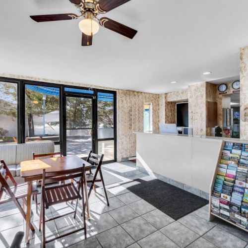 A small room with a table, chairs, brochures on a rack, and windows. There is also a ceiling fan and tiled floor, creating a cozy setting.