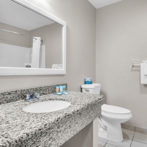A clean bathroom with a granite countertop, sink, toilet, mirror, shower, and towels.